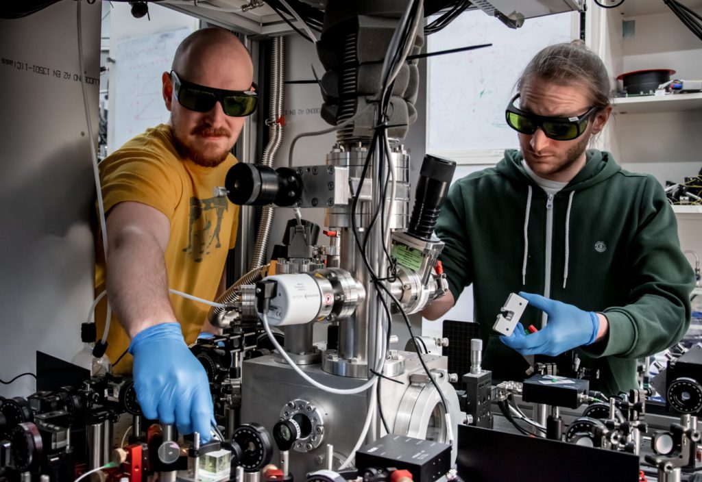 کاهان دره(Kahan Dare) در سمت چپ و مانوئل رایزنباور(Manuel Reisenbauer) در سمت راست، محققان آزمایشگاه مارکوس آسپلمایر ، بر روی این آزمایش کار می کنند تا نانوذره ای را که به حالت کوانتومی در آمده است، خنک کند.